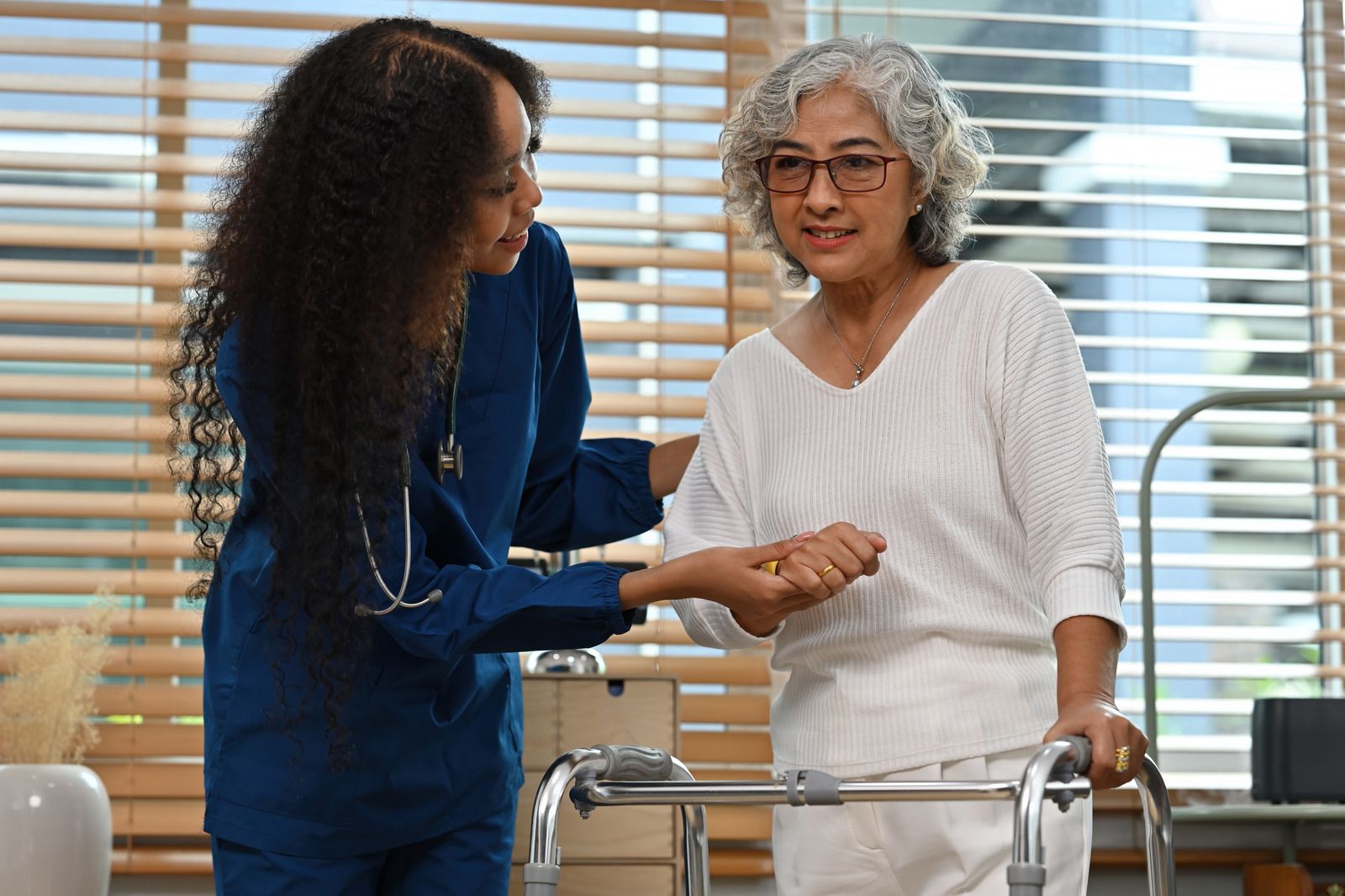 Woman in wheelchair with two medical professionals in a hospital hallway.