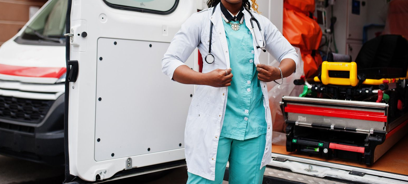 Woman in scrubs holding hands with an elderly woman, smiling, in a bedroom.