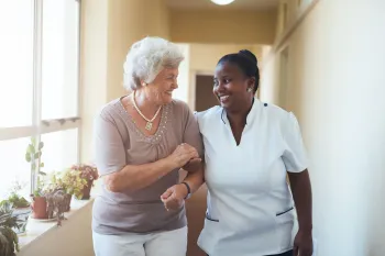 Caregiver holding hands with senior, smiling, in a bedroom setting.