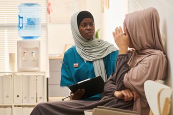 Smiling healthcare worker in blue scrubs with team in background.