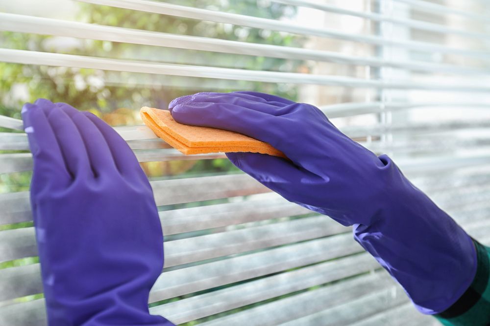 A Person Wearing Purple Gloves Is Cleaning Blinds With An Orange Cloth — AGB Cleaning In Tablelands, QLD