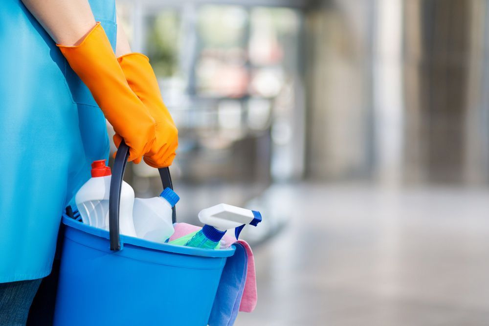 A Person Wearing Orange Gloves Is Holding A Blue Bucket Filled With Cleaning Supplies — AGB Cleaning In Bentley Park, QLD