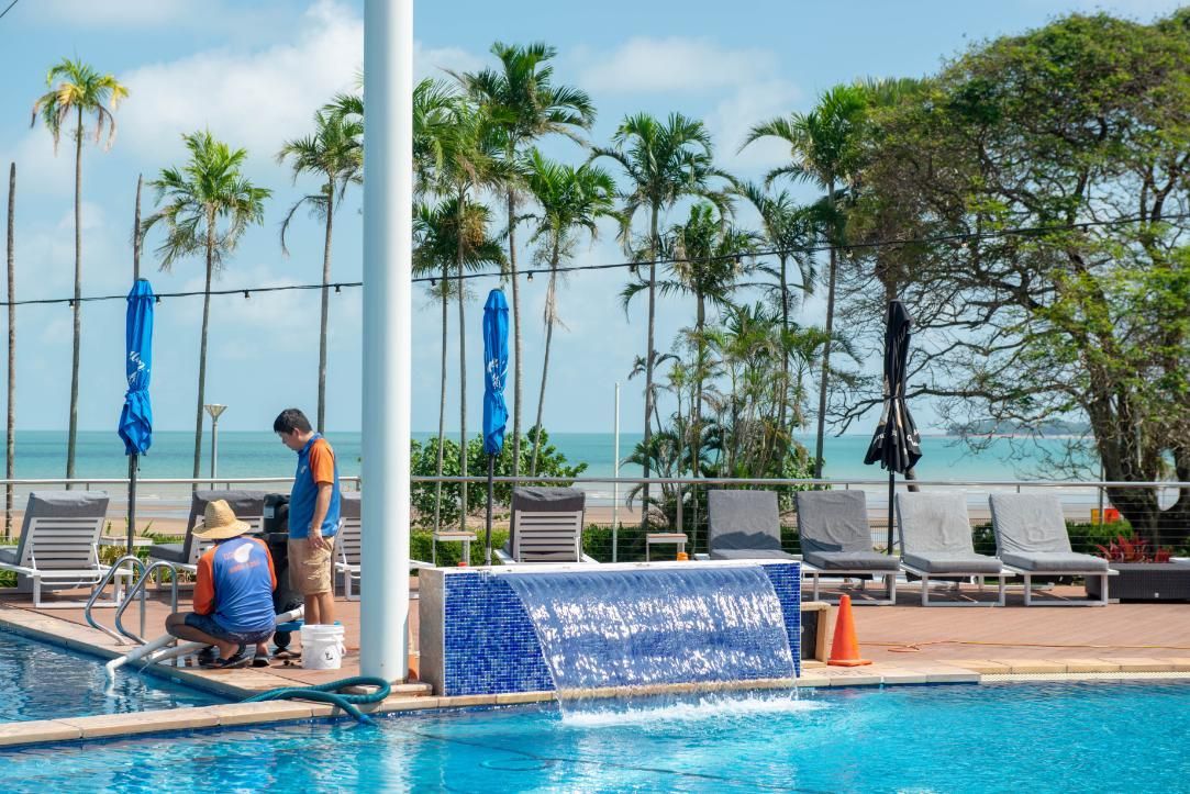 A Man Is Standing Next to A Swimming Pool with Palm Trees in The Background — Figleaf Pool Products in Coconut Grove, NT