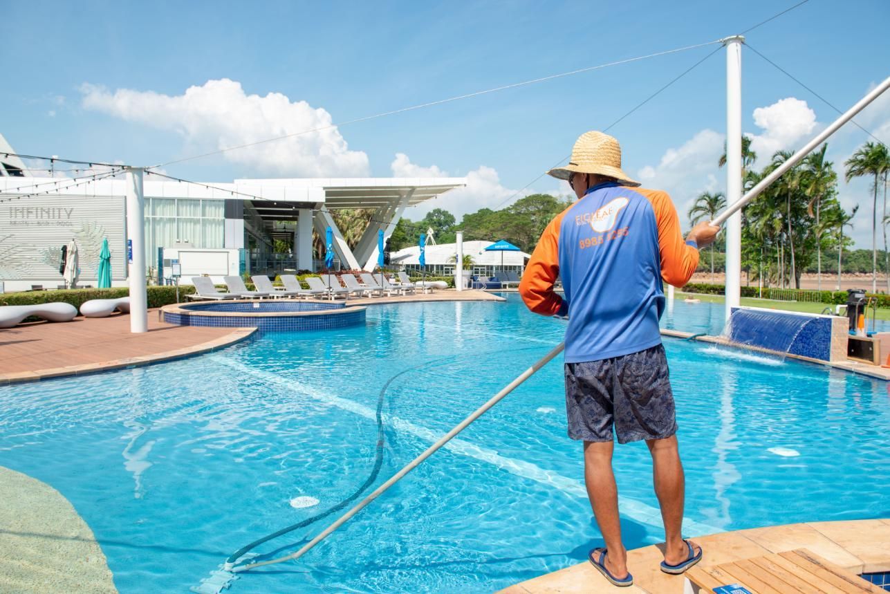 A Man Is Cleaning a Swimming Pool with A Broom — Figleaf Pool Products in Coconut Grove, NT