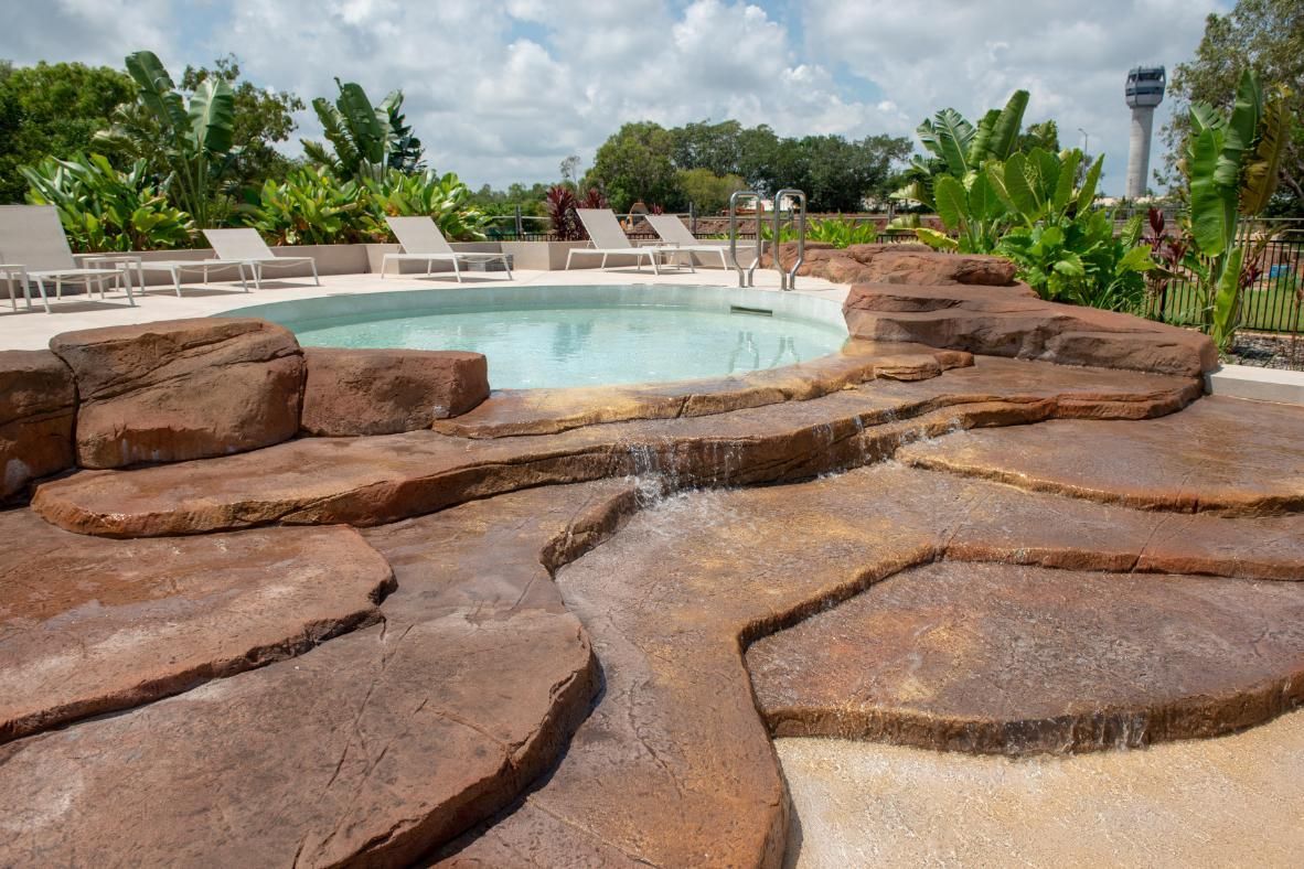 A Man Is Working on A Swimming Pool with A Waterfall in The Background — Figleaf Pool Products in Coconut Grove, NT