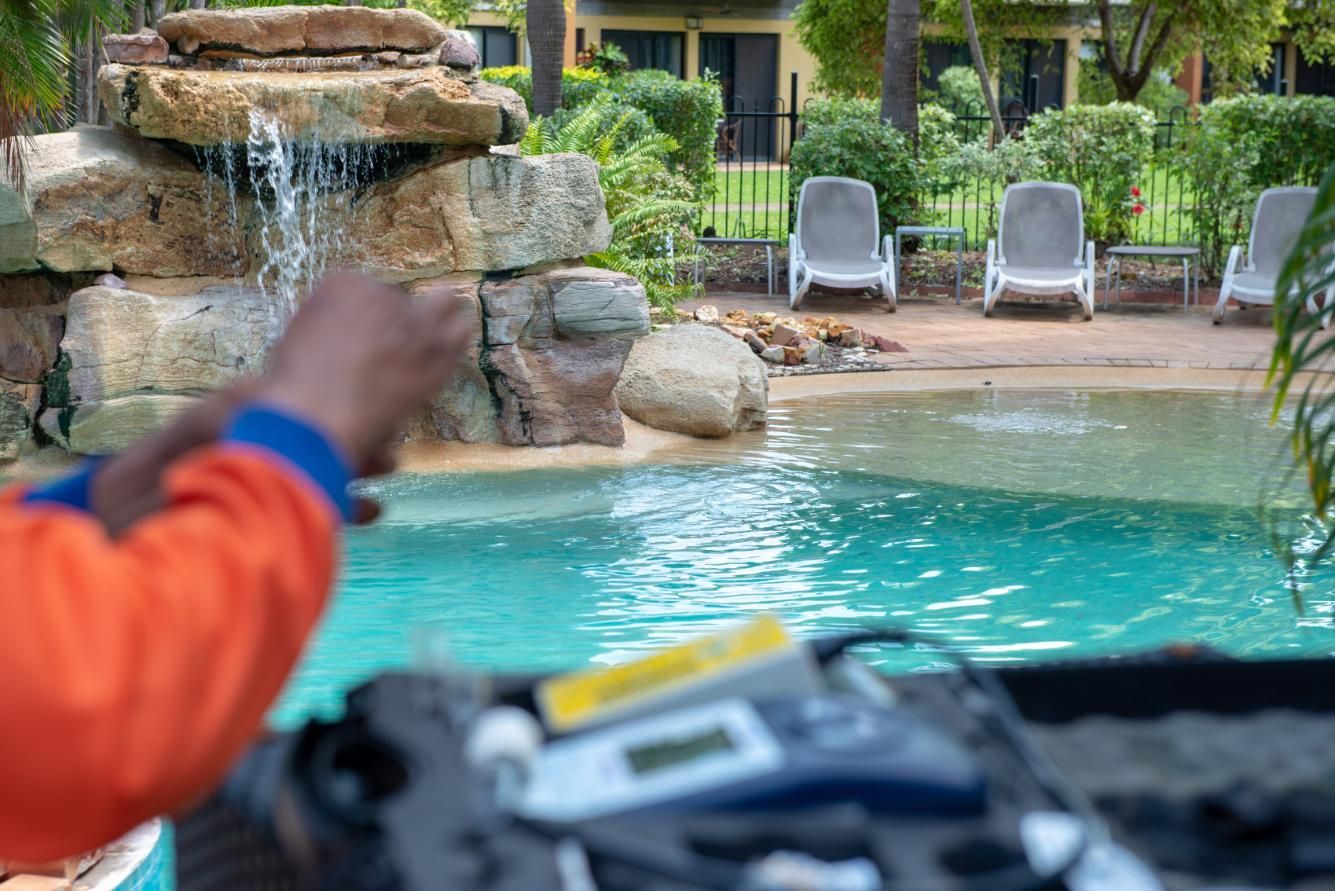 A Man Is Working on A Swimming Pool with A Waterfall in The Background — Figleaf Pool Products in Coconut Grove, NT