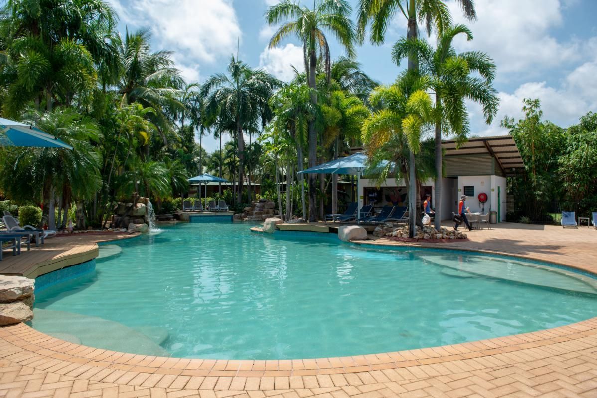 A Large Swimming Pool Surrounded by Palm Trees and Umbrellas  — Figleaf Pool Products in Coconut Grove, NT