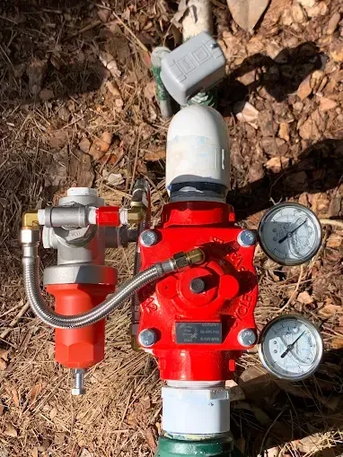 Red water pressure regulator with gauges, filter, and connection in outdoor setting.