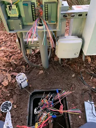 Open utility box with tangled wires; conduit leads to a ground-level box.