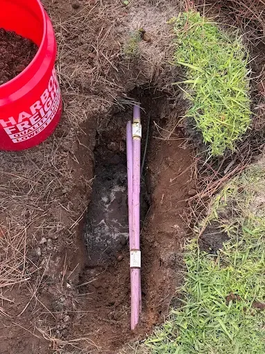 A partially dug hole with purple pipes and a red bucket.