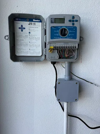 Gray Hunter irrigation controller mounted on a white wall, with open door revealing wiring.
