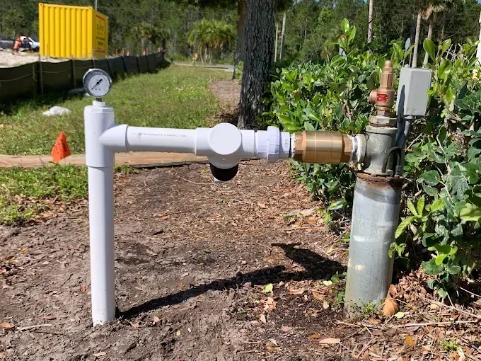Water well system with pressure gauge, pipes, and valve in an outdoor setting.
