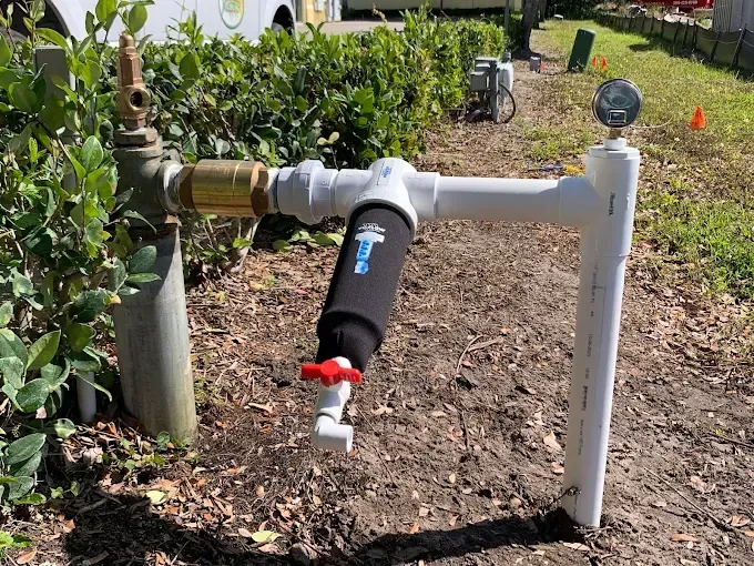 Water filtration system with black filter, white pipes, and a pressure gauge outdoors.