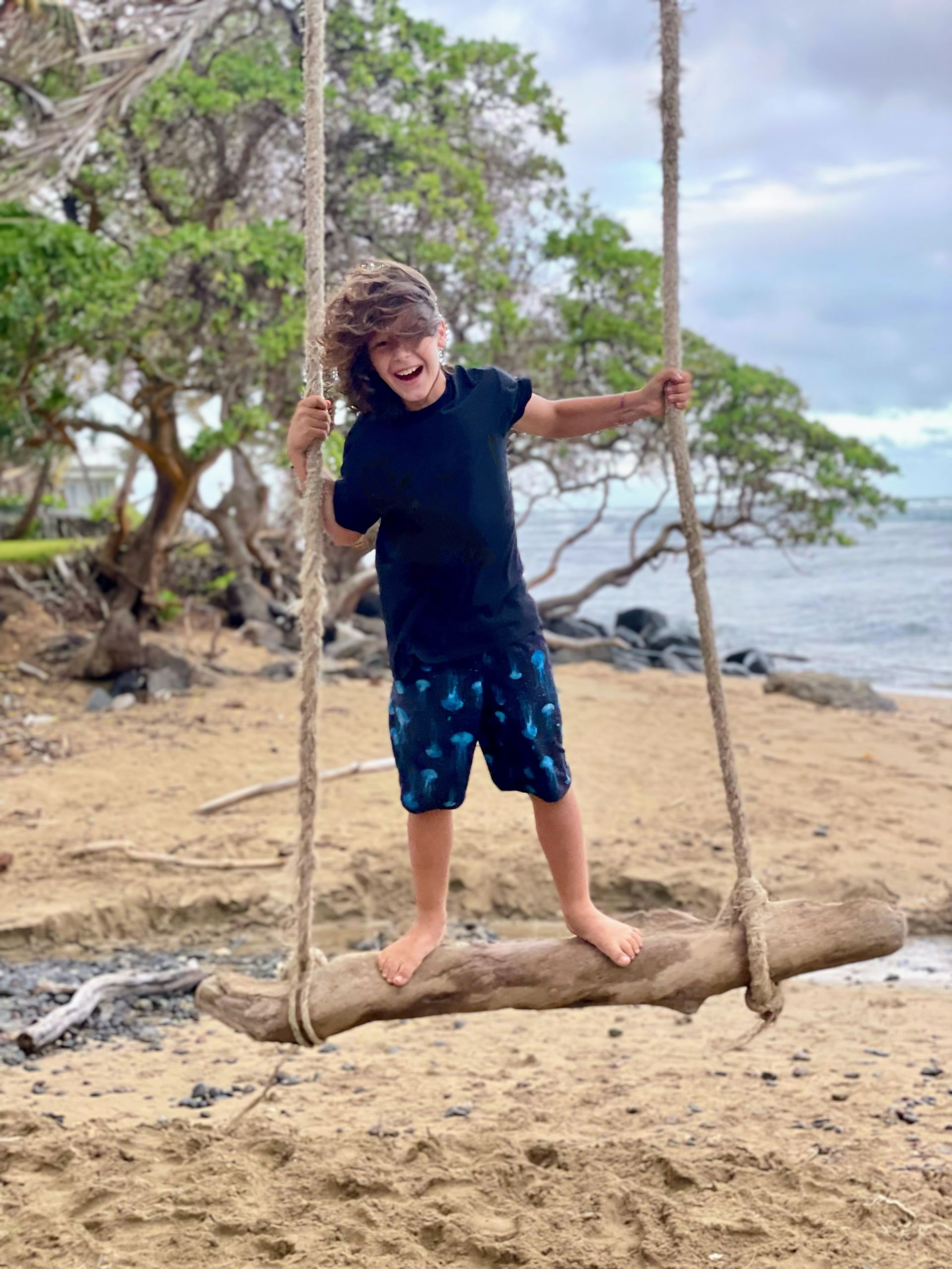 Cute boy swinging on a rope swing on the beach in Hawaii