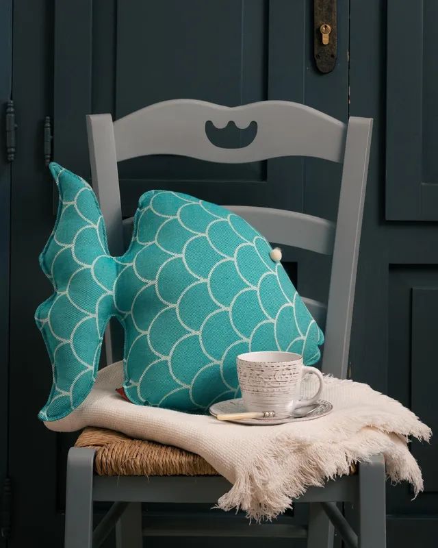 Un cuscino a forma di pesce è seduto su una sedia accanto a una tazza di caffè.