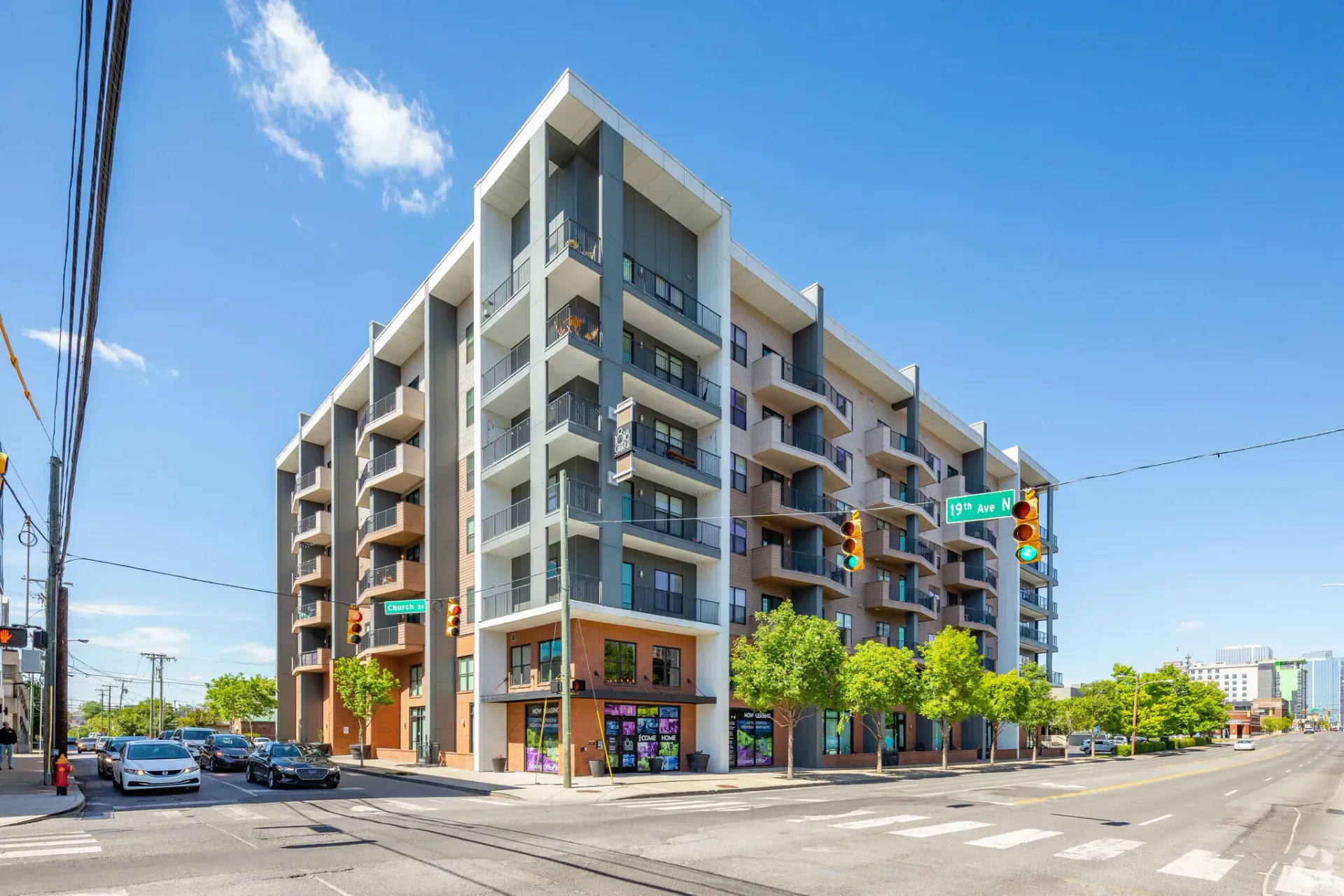 Exterior view of a modern multi-story apartment building with balconies on a street corner.