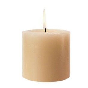 Tan pillar candle burning with a small flame, against a white background.