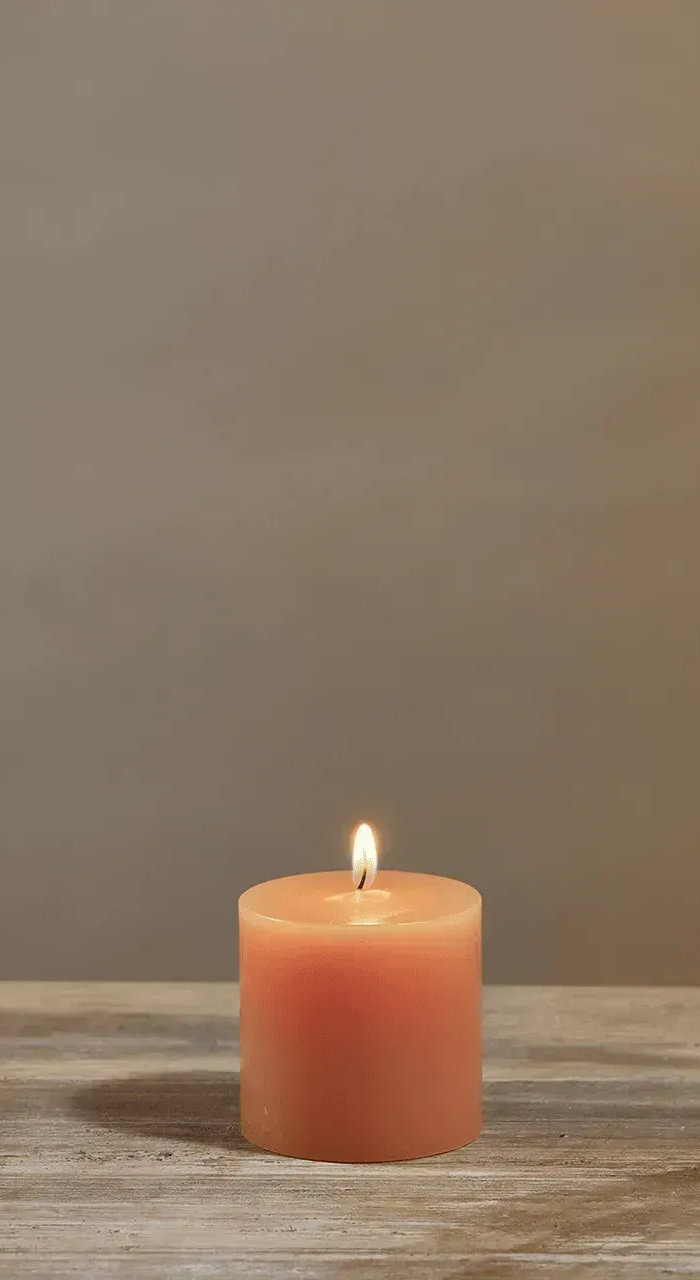 Lit orange candle on a wooden surface against a neutral background.