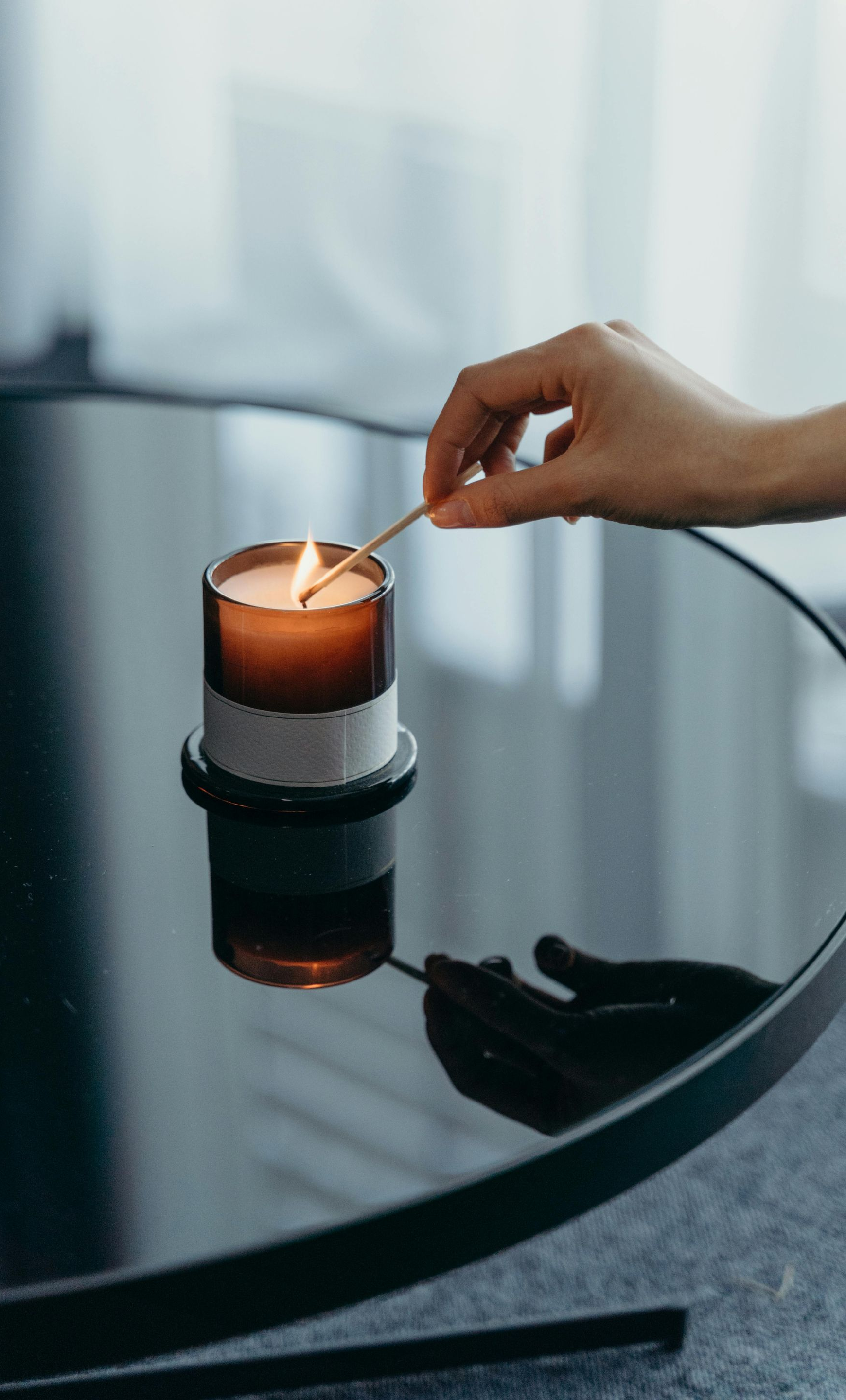 Hand lighting a brown candle on a black, reflective table.