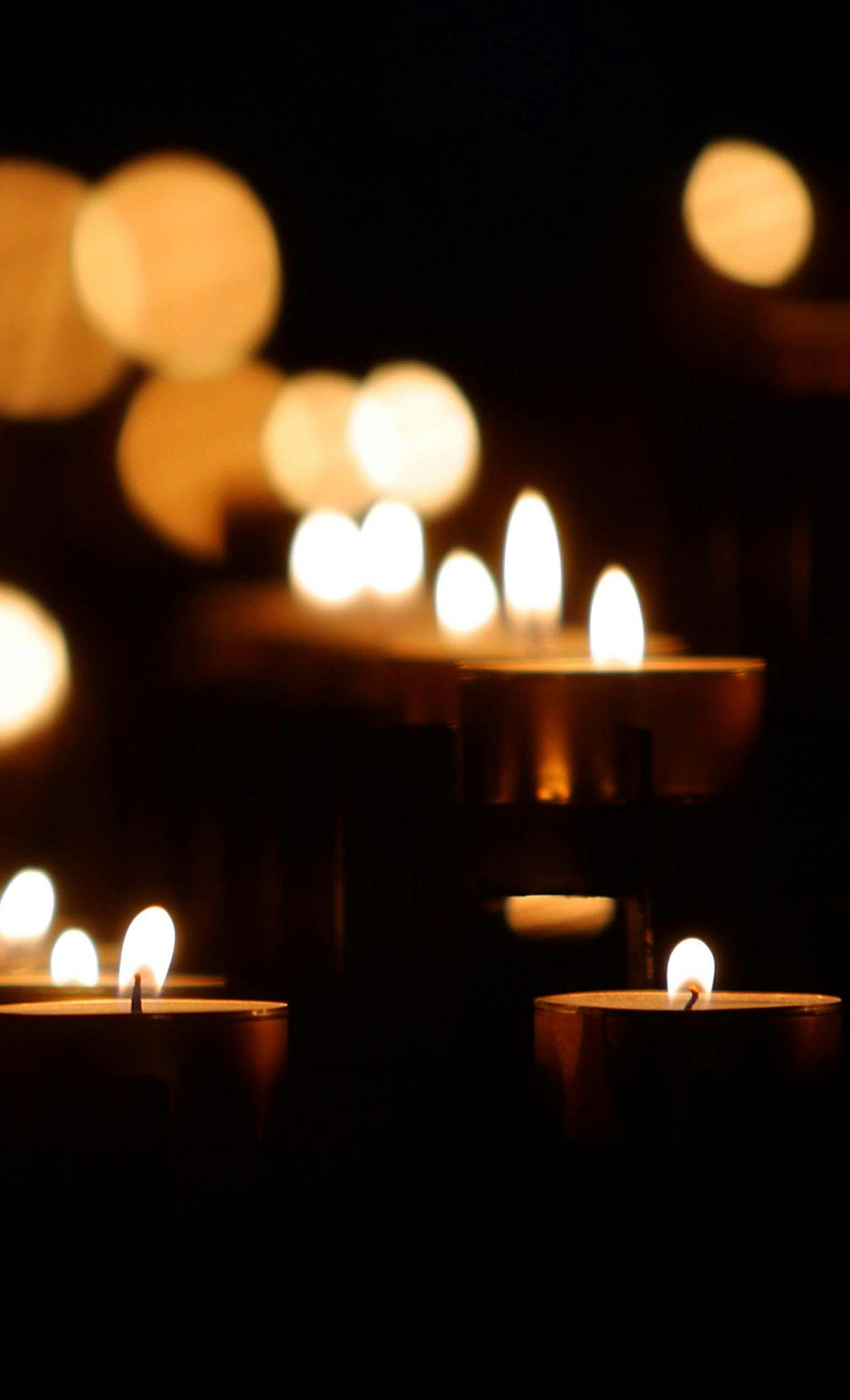 Candle flames glow in the dark, soft focus on gold tealights. Bokeh effect in background.