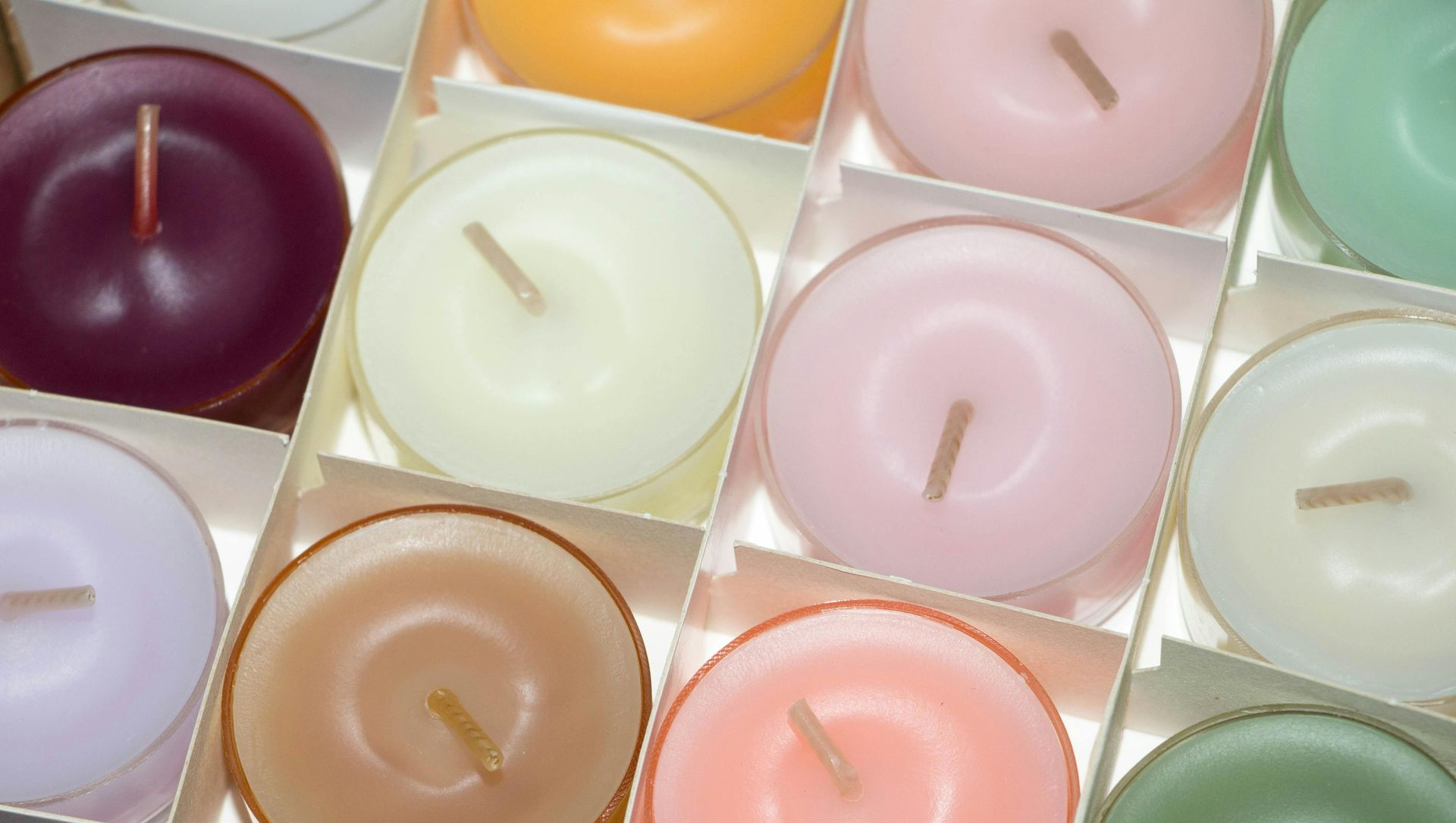 Close-up of a box of colorful, round tea light candles: purple, yellow, pink, green, and cream.