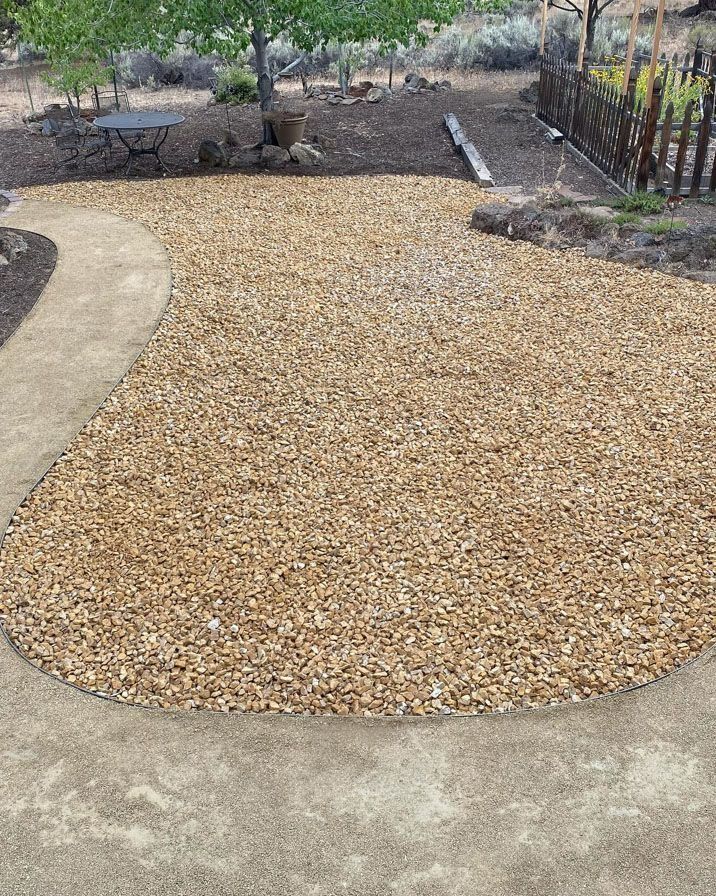 Gravel patio with a curving path and a small table under trees.