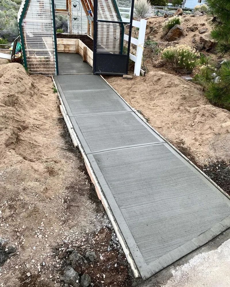 Concrete ramp leading to a greenhouse, bordered by dirt.