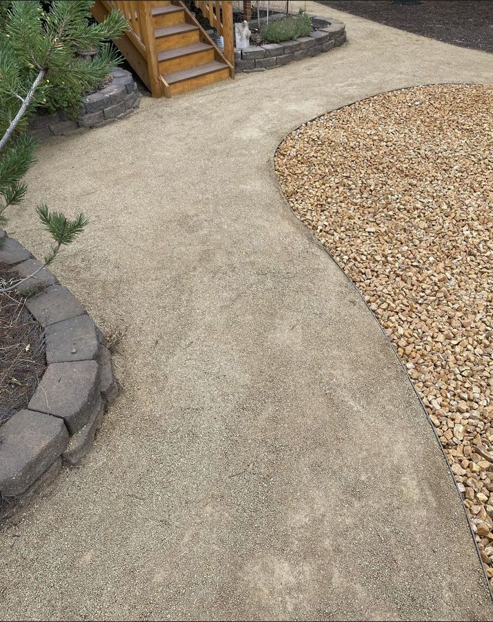 A winding pathway of beige gravel beside a rock border and a section of brown pebbles leading to wooden stairs.