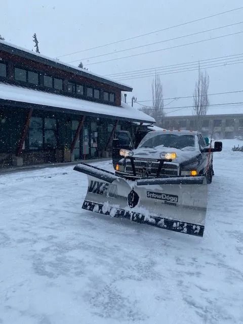 Snowplow clearing snow in front of a building with falling snow.