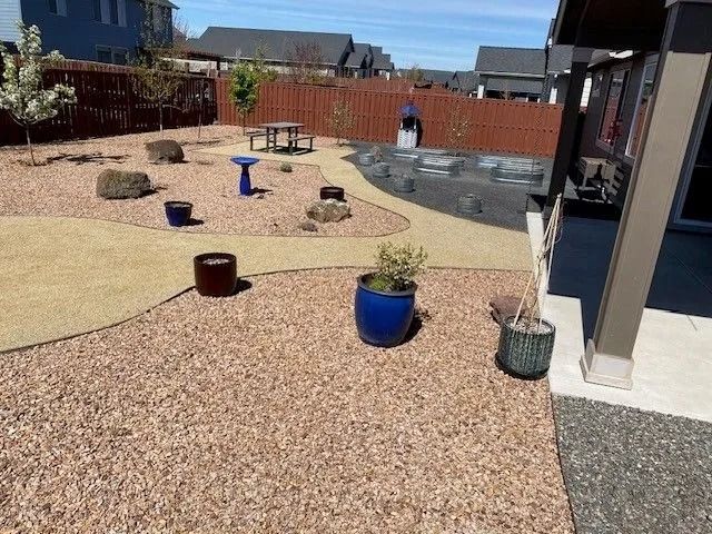 A backyard with gravel paths, decorative rocks, and potted plants, near a fence.