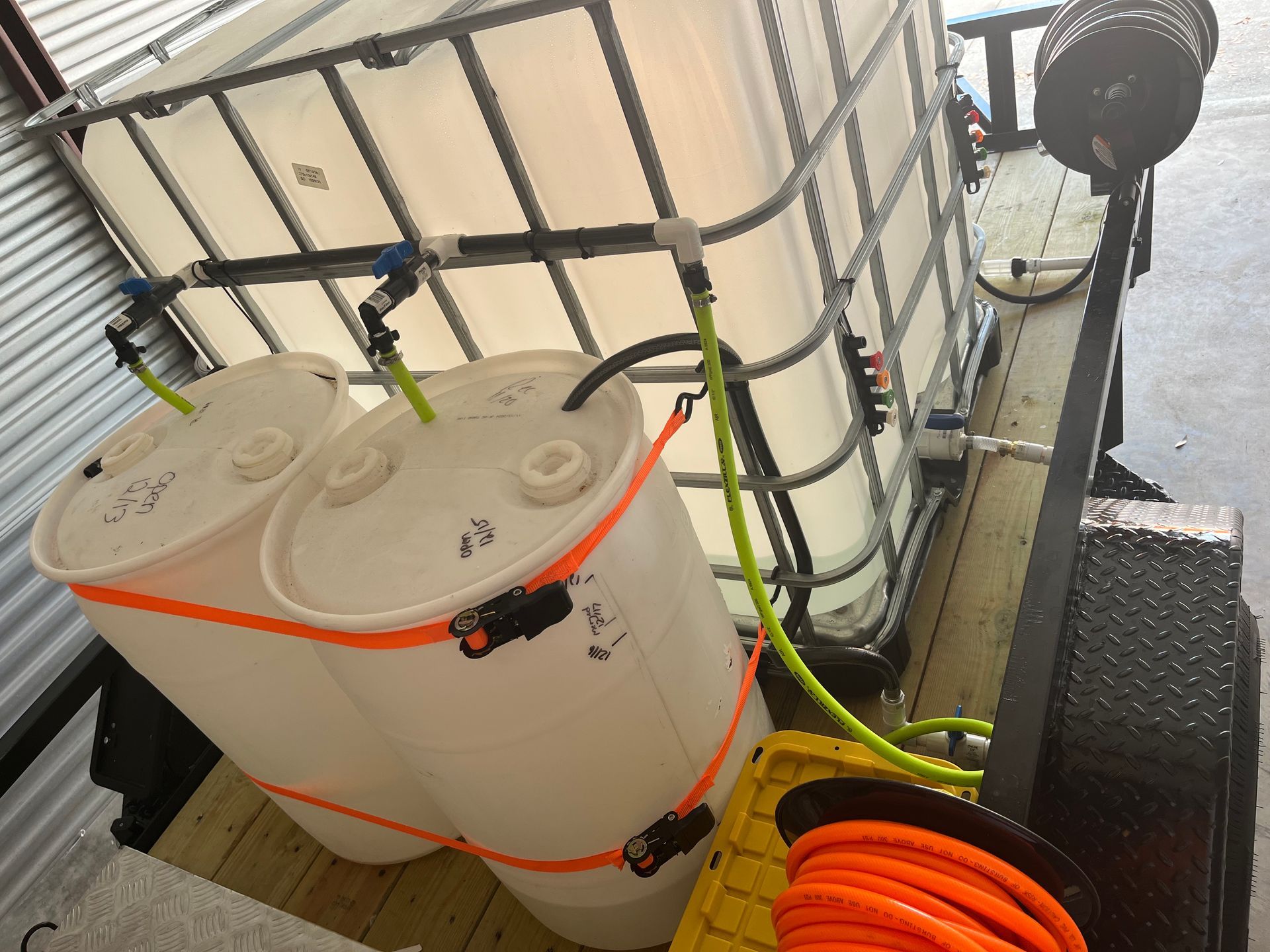 A trailer holding white tanks for water and chemicals, with hoses and a pump.