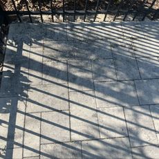 A fence casts a shadow on a brick walkway