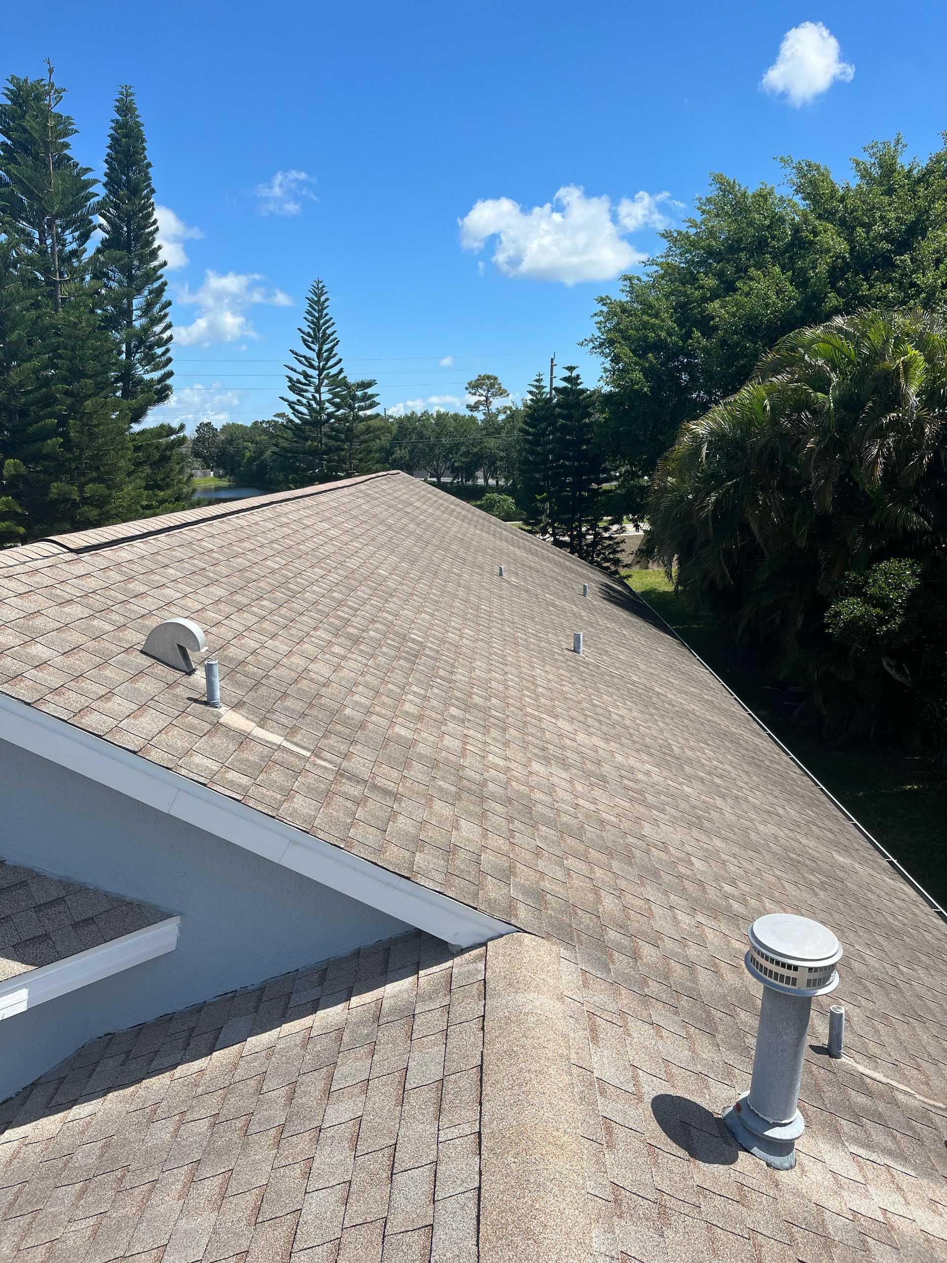 The roof of a house with a blue sky and trees in the background.