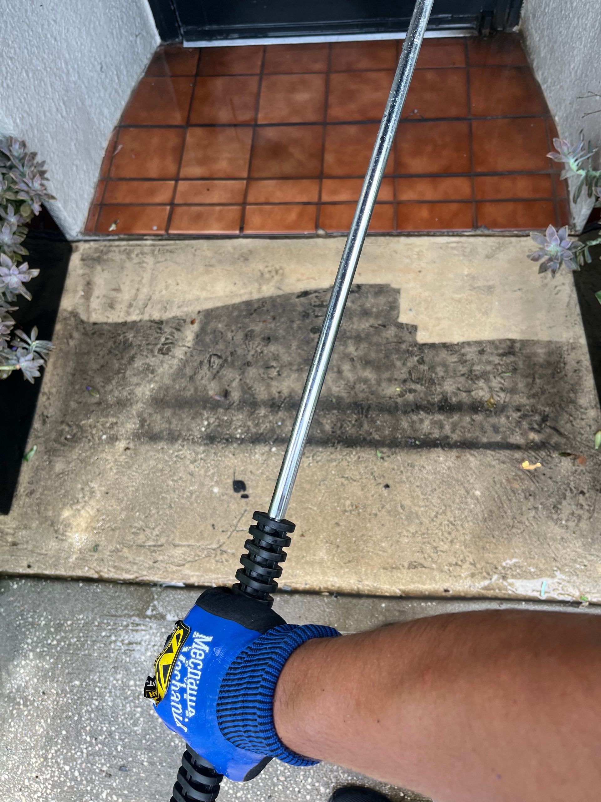 Person power washing a concrete entryway, revealing clean path.