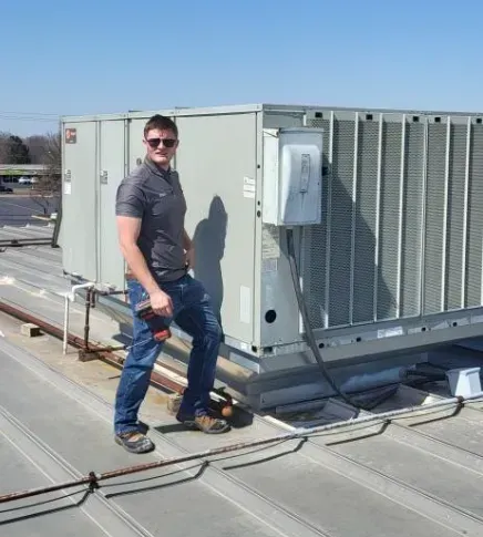 A man is standing on top of a roof next to an air conditioner.