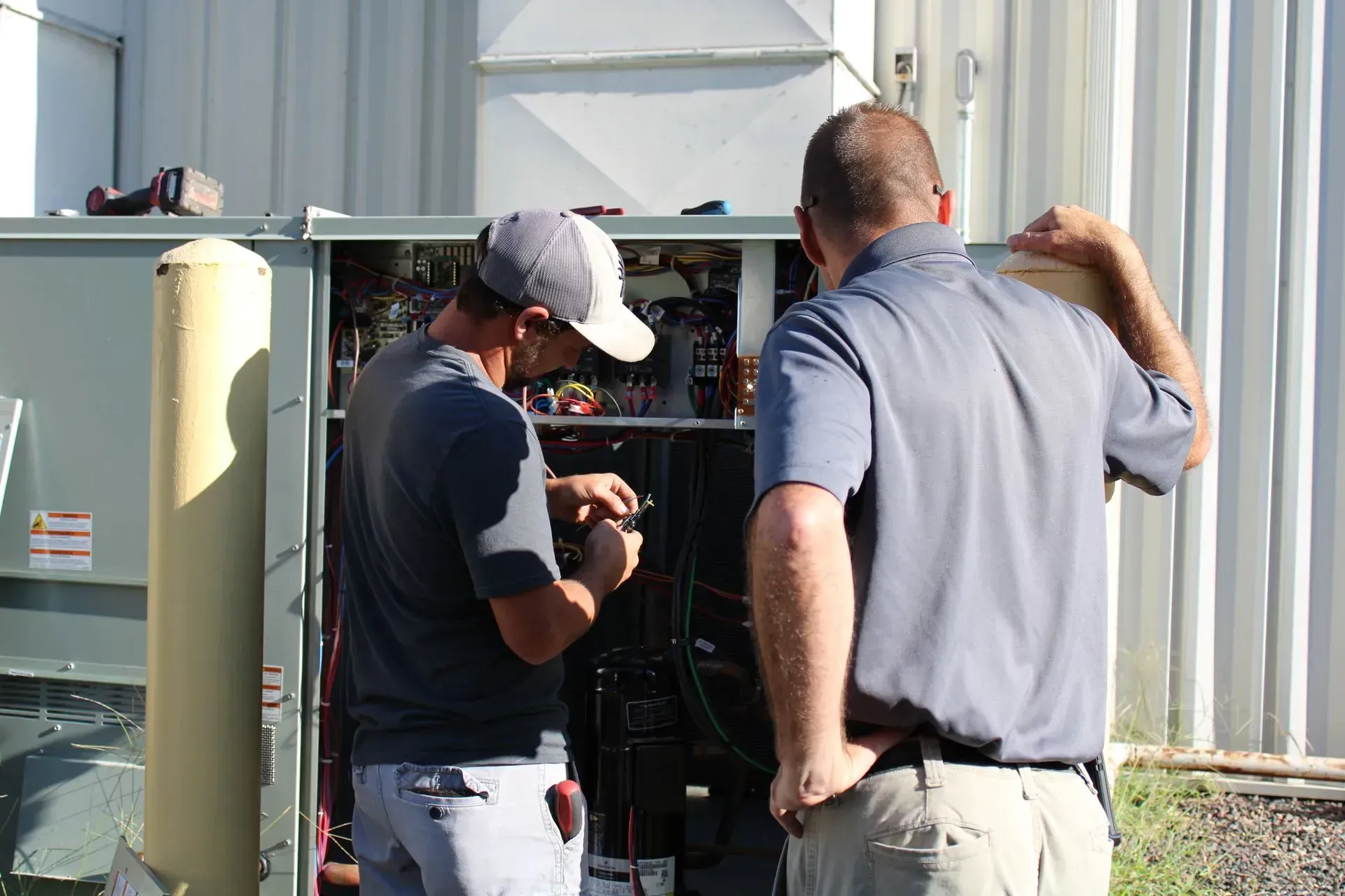 Two men are working on a machine outside of a building.