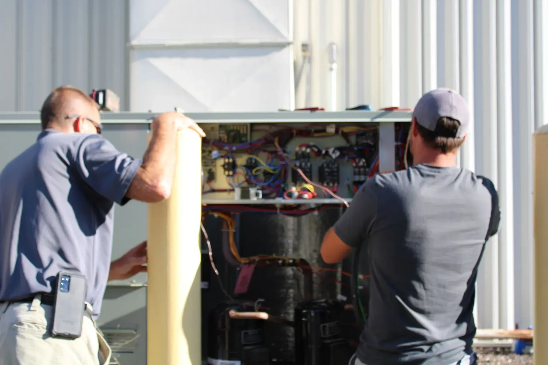 Two men are working on an air conditioner outside of a building.