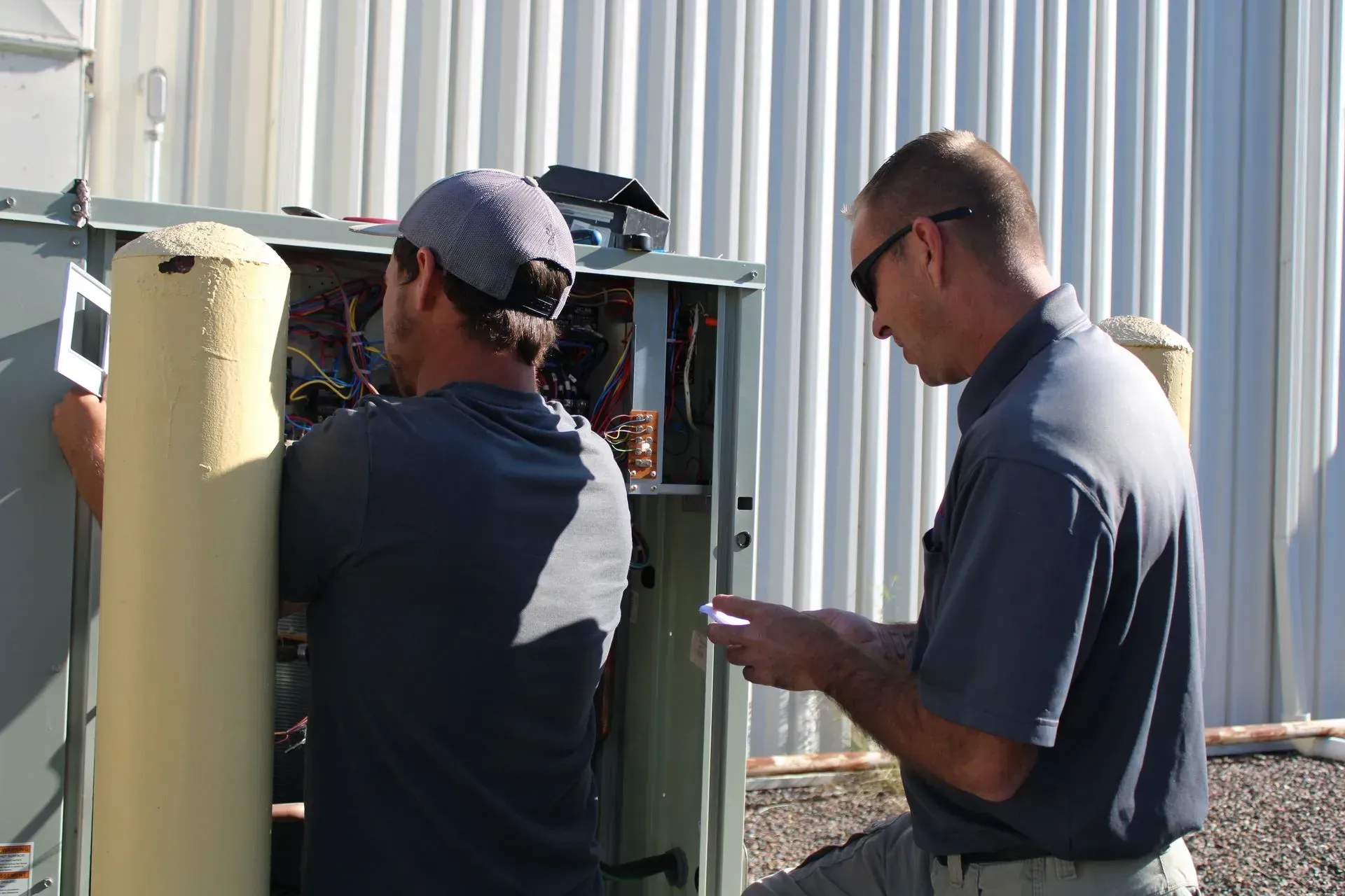 Two men are working on an electrical box in front of a building.