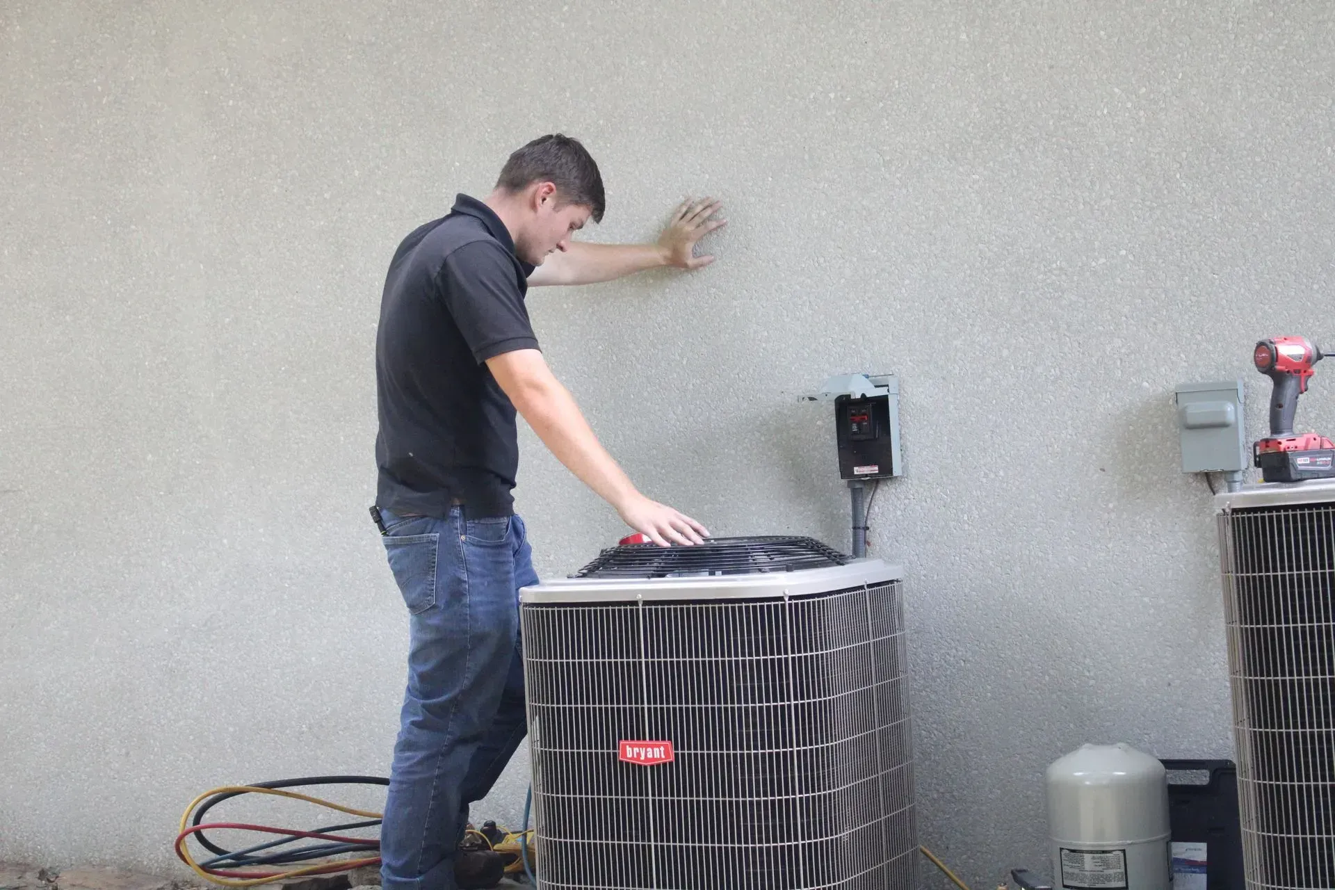 A man is working on an air conditioner outside of a building.