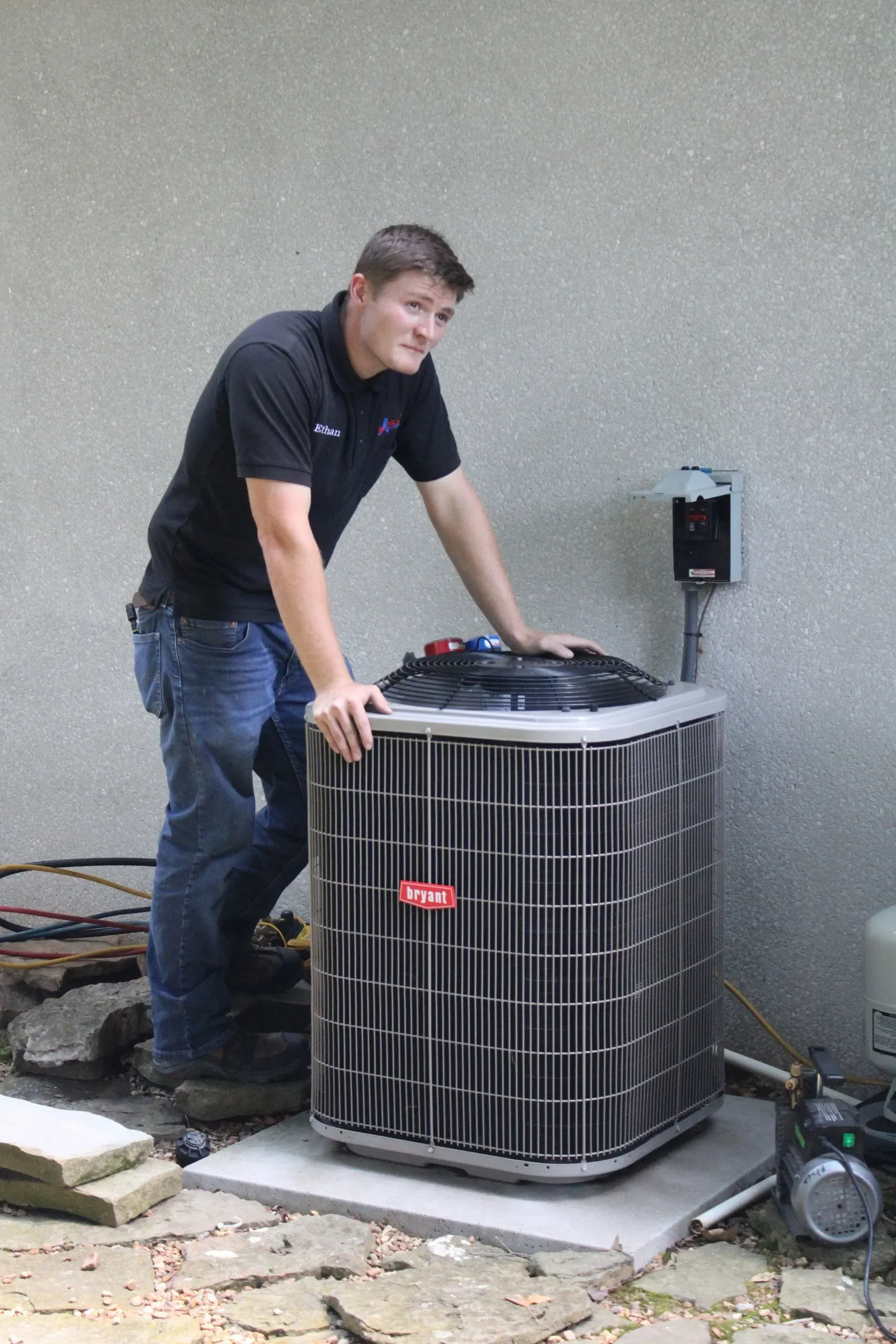 A man in a black shirt is standing next to an air conditioner.