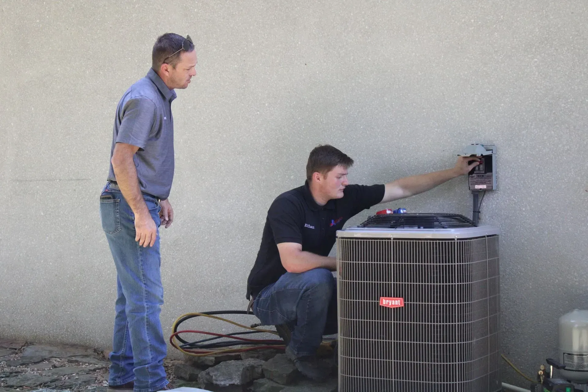 Two men are working on an air conditioner outside of a building.