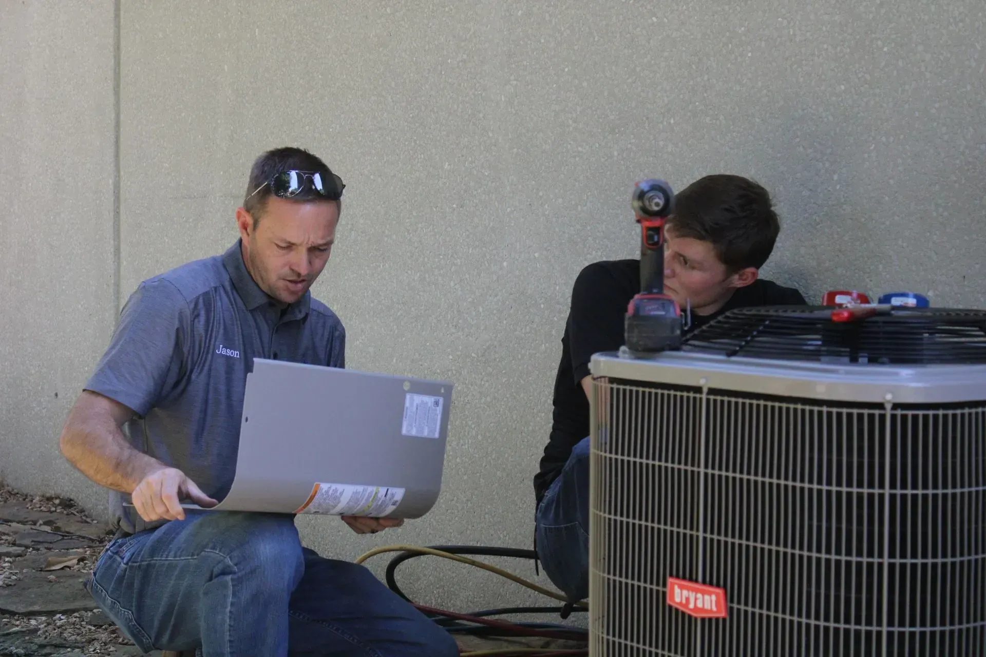 Two men are working on an air conditioner outside of a building.