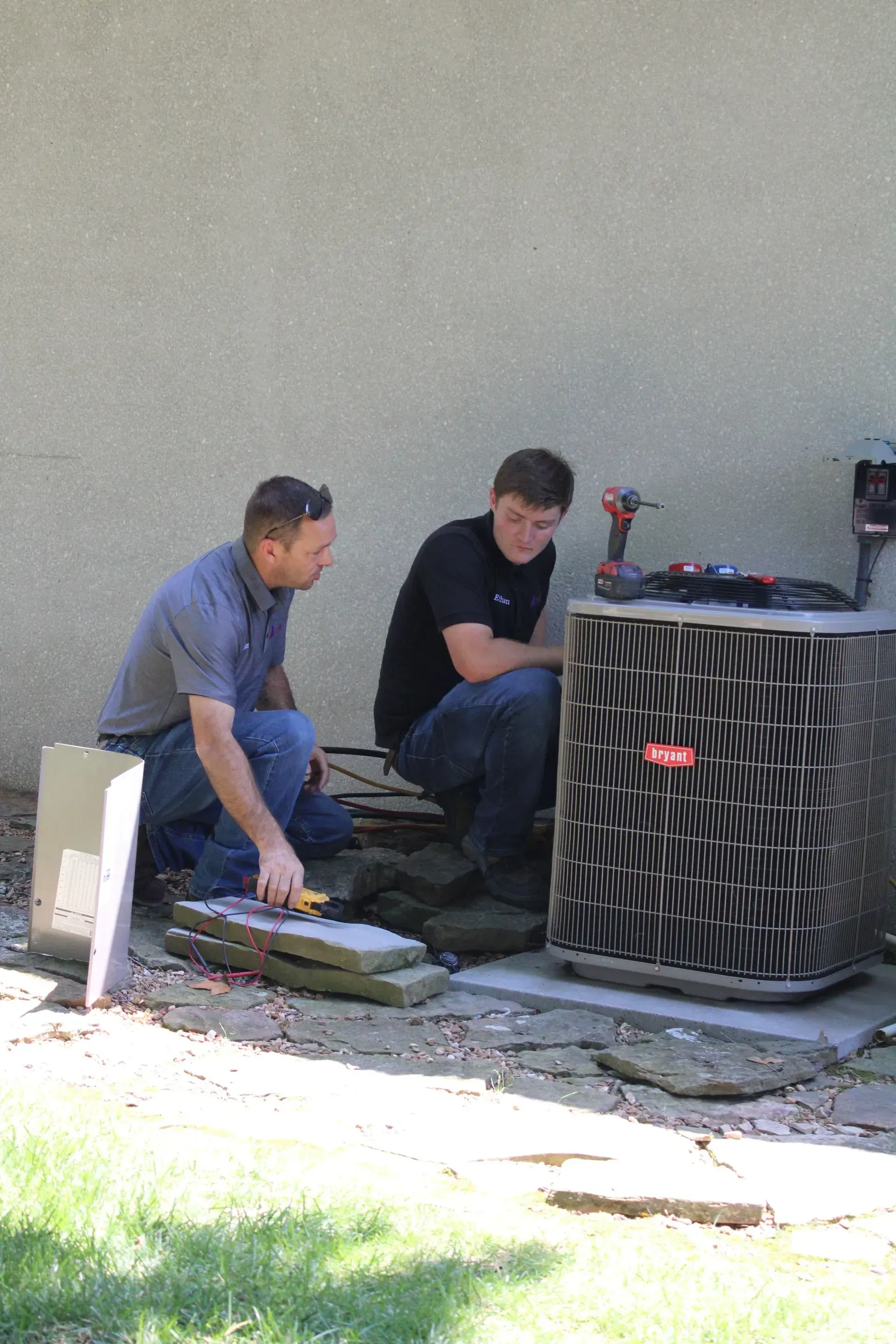 Two men are working on an air conditioner outside of a house.