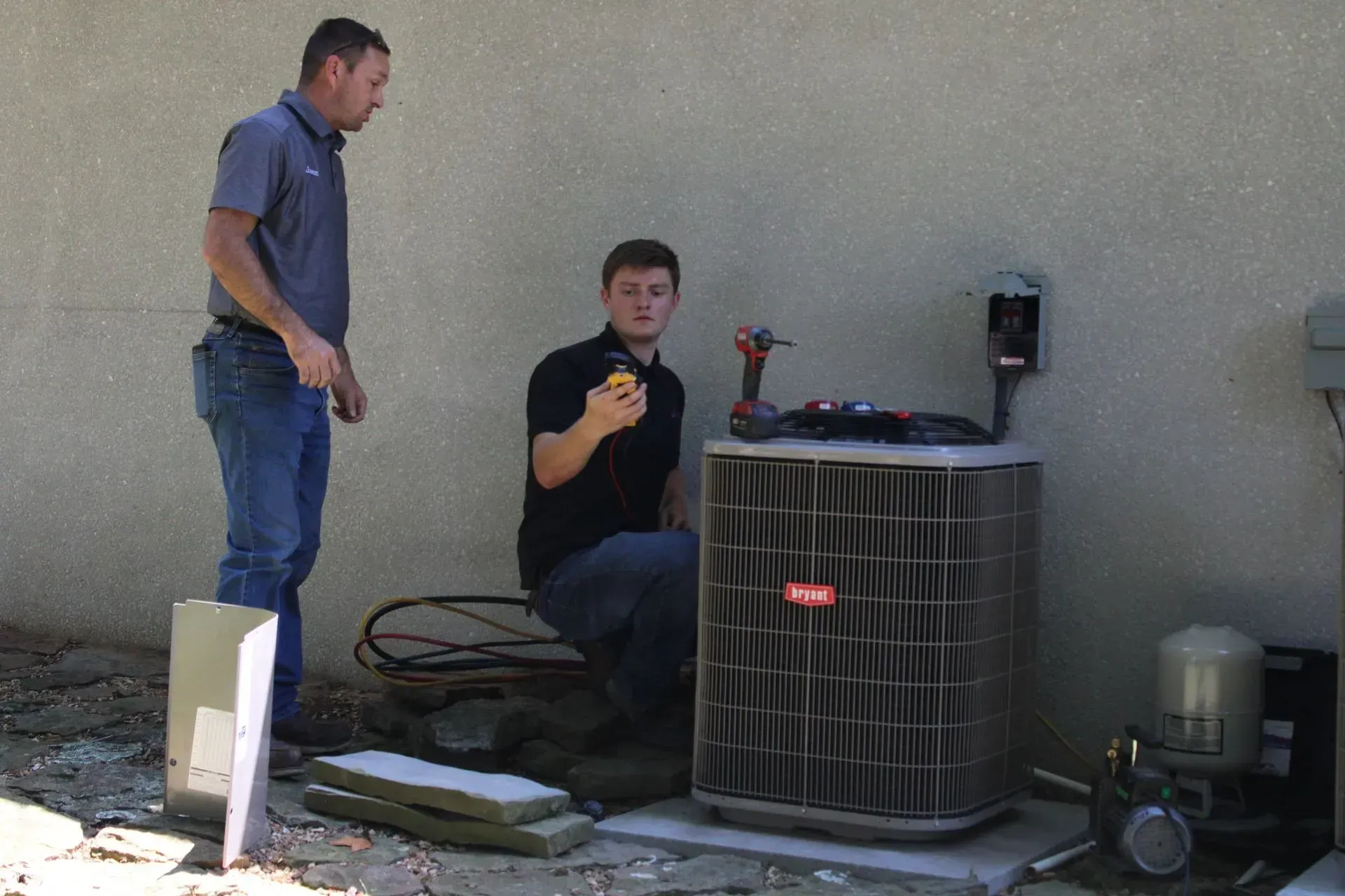 Two men are working on an air conditioner outside of a building.