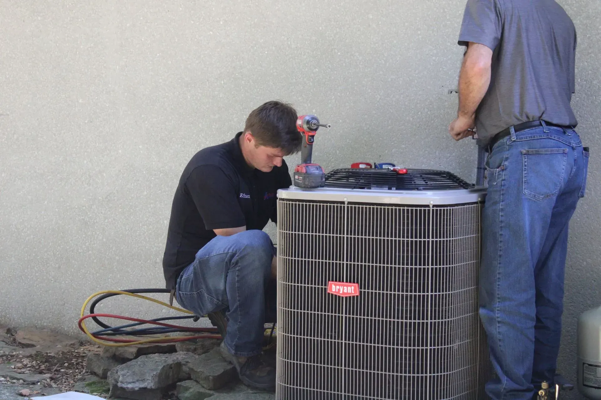 Two men are working on an air conditioner outside of a building.