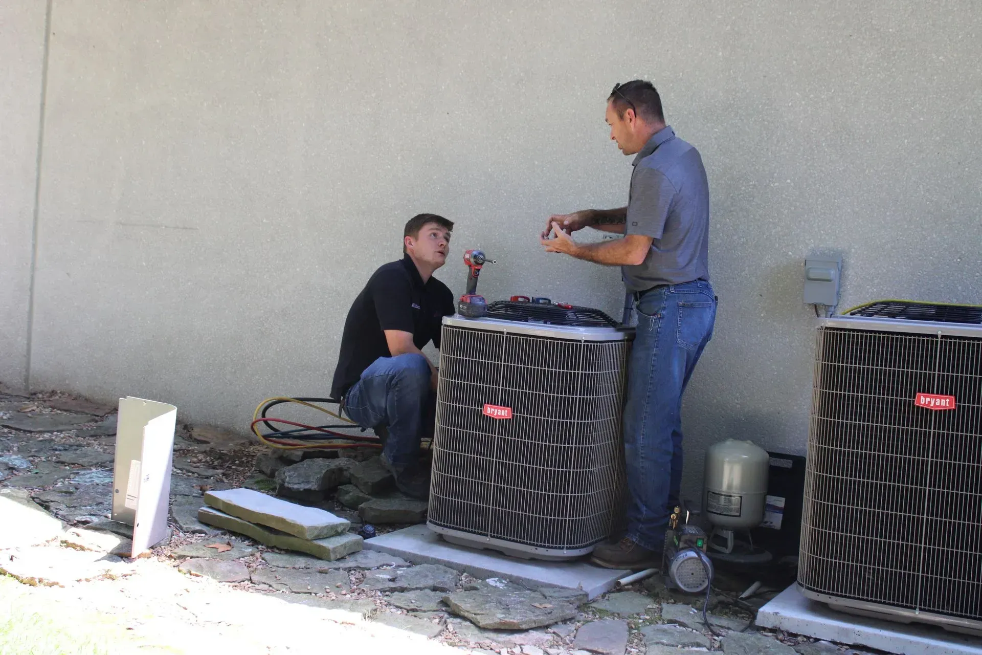 Two men are working on an air conditioner outside of a building.