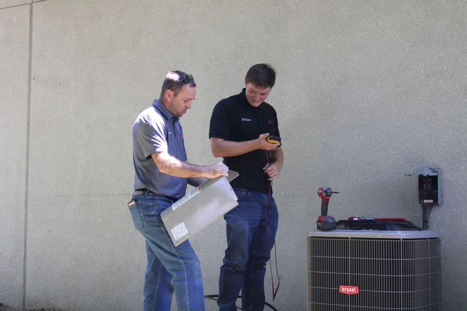 Two men are working on an air conditioner outside of a building