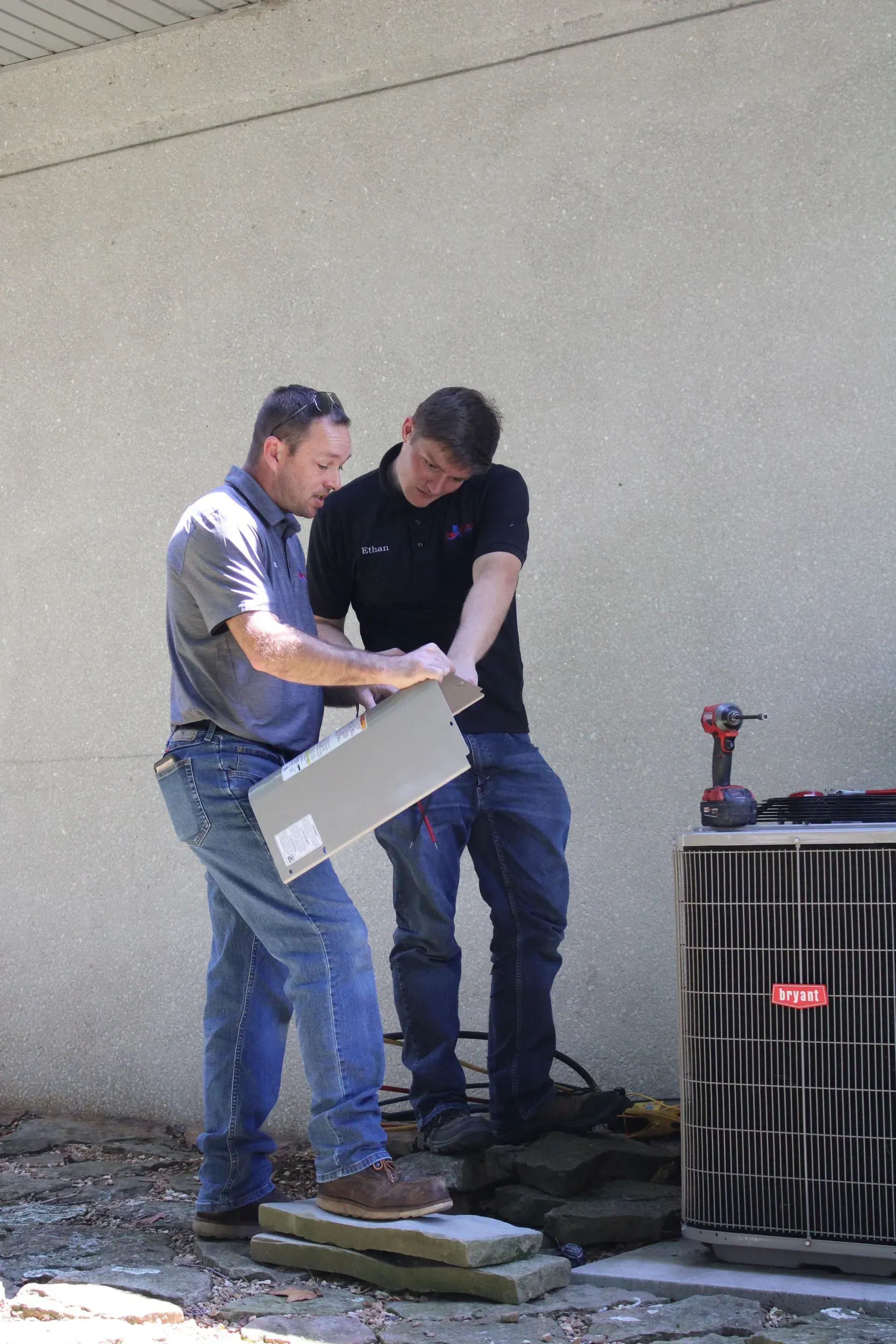 Two men are working on an air conditioner outside of a building.