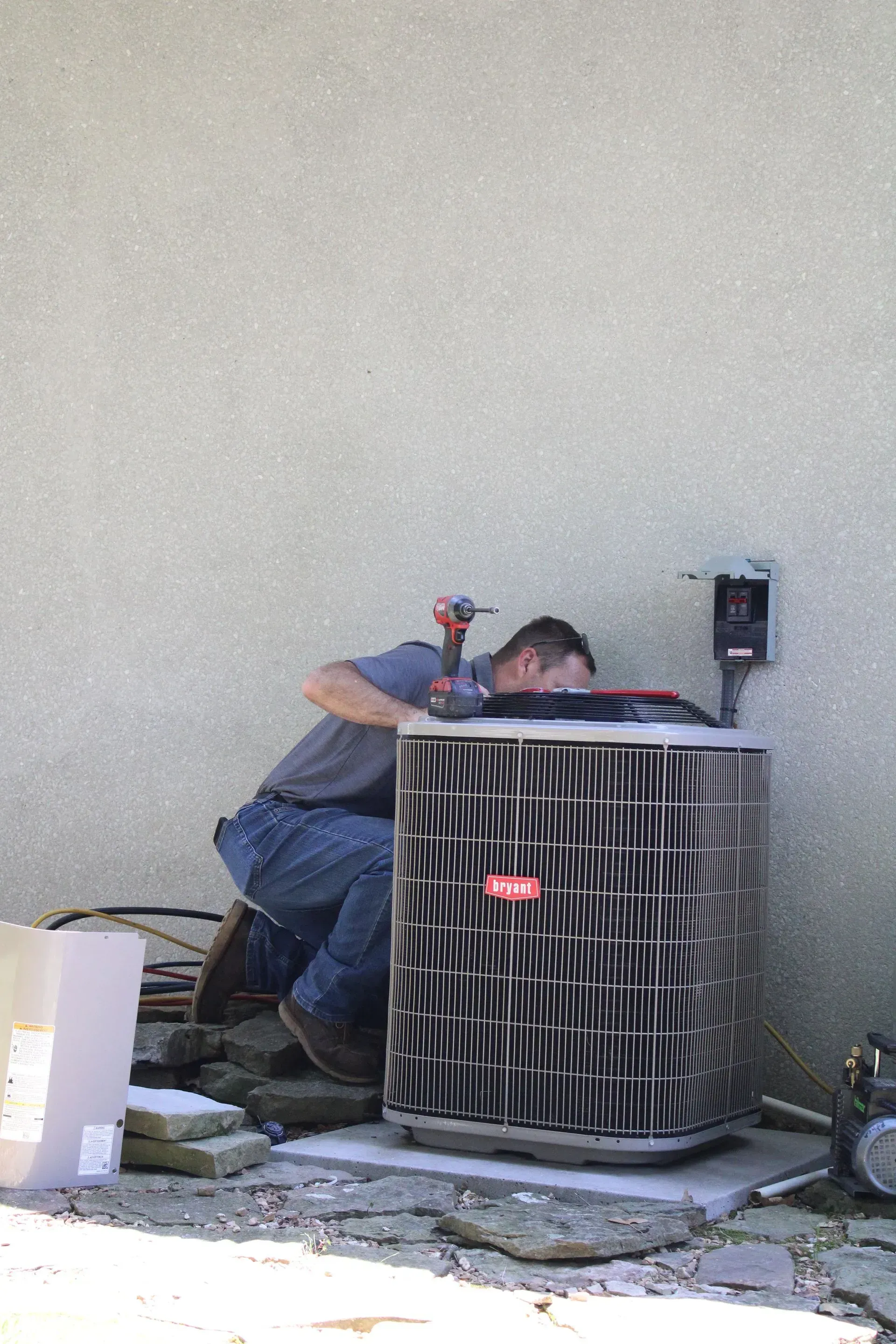 A man is working on an air conditioner outside of a building.