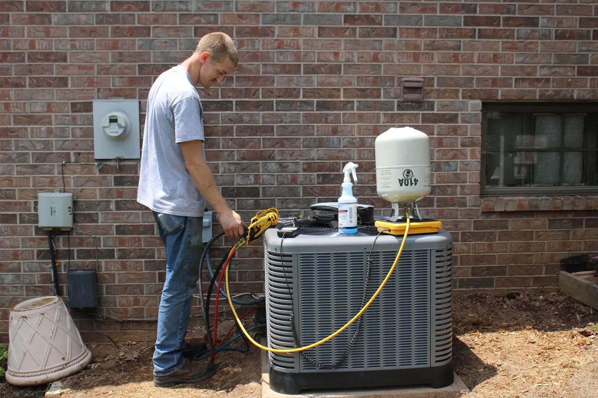 A man is working on an air conditioner outside of a brick building.